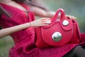 mini red leather hand bag in hands of mannequin doll sitting in the grass in a public garden