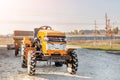 Mini red tractor with trailer standing near hangar building at farm during sunset or sunrise. Small agricultural