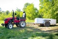 Mini red tractor with trailer standing near hangar building at farm during sunset or sunrise. Small agricultural machinery. Rural Royalty Free Stock Photo