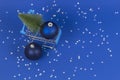 Mini shopping cart with small Christmas tree and navy Christmas decoration bauble balls on blue background with silver Royalty Free Stock Photo