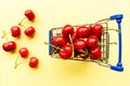 Mini shopping grocery cart full of fresh cherries. Fresh berries on yellow background. Healthy, summer food concept. Top Royalty Free Stock Photo