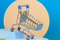 Mini shopping trolley cart with geometric beige and light blue podium platforms. Online shopping, supermarket background Royalty Free Stock Photo