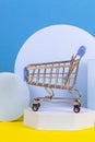 Mini shopping trolley cart with geometric podium platforms on yellow and light blue background. Online shopping concept Royalty Free Stock Photo