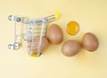 A mini shopping trolley with speckled chicken eggs and yolk on a neutral background