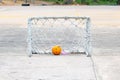 Mini soccer goal with old and rust condition broken net on concrete soccer field in park with small dark yellow ball. Royalty Free Stock Photo