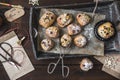 Mini stollen with sugar icing on a wooden tray, paper bags, scissors, pen holder and gift ribbon on dark wood