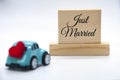 Mini toy car carrying red heart shape with Just Married text on wooden blocks background. Newly wed concept. Royalty Free Stock Photo