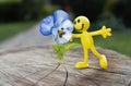 Miniature bright toy figure of a yellow cheerful little people near a pansy flower. concept of love, joy, happiness