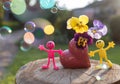 Miniature bright toy figurines of people near heart-shaped vase with pansies, bubbles beautifully illuminated by sun