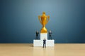 Miniature business concept - businessman standing in front of white winner podium with golden trophy Royalty Free Stock Photo
