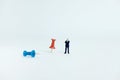 Miniature business concept - a businessman standing beside red and blue thumbtack push pin with white background