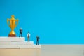 Miniature business concept - businessman standing on white winner podium with golden and silver trophy Royalty Free Stock Photo