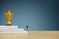 Miniature business concept - businessman walking on white staircase ladder to reach golden trophy Royalty Free Stock Photo
