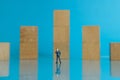 Miniature business concept - thinking young businessman standing in front of wooden chart