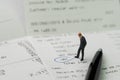 Miniature business man figurine standing on printed payment invoice, bill or receipt and looking at VAT with pen circle using as