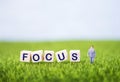 Miniature business man with focus word on wooden cube on green grass with space on blurred background