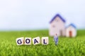 Miniature business man with goal word on wooden cube on green grass with space on blurred backgroun