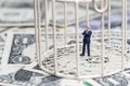 Miniature businessman inside birdcage on pile of dollar banknote