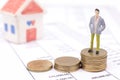 Miniature businessman and stack coins on statement and the house