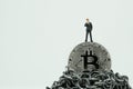 Miniature businessman standing on Bitcoin on top of chain mountain thinking about high future value