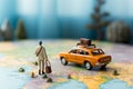 Miniature businessman, suitcase, and handbag sprint near a colorful world map and mini car