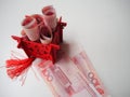 Miniature Chinese pavilion in bright red filled with Chinese 100 renminbi banknotes against a white background