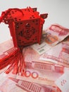 Miniature Chinese pavilion in bright red standing on Chinese 100 renminbi banknotes against a white background