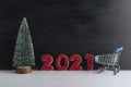 Miniature Christmas tree, trolley cart and inscription 2021 on black background. New Year discounts, shopping