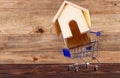 Miniature decorative wooden house in a shopping cart trolley on wood background