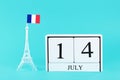 Miniature of the Eiffel Tower with a French flag and wooden calendar on a blue background. The concept of the holiday is July 14, Royalty Free Stock Photo