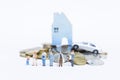 Miniature family and business man with old man and couple over blurred stack of coins with house and car on white background