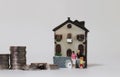 A miniature family standing in front of a miniature house and a pile of coins. Royalty Free Stock Photo