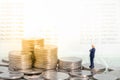 Miniature figure businessman stand on pile of coins thinking and looking to stack of coins with bank passbook as background. Royalty Free Stock Photo