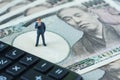 miniature figure businessman thinking standing on pile of japanese yen banknotes and calculator as financial safe haven or tax co Royalty Free Stock Photo