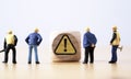 Miniature figure of senior engineer standing and see at warning exclamation caution sign for notification maintenance and