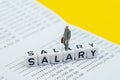 Miniature figure working businessman, office guy walking on cube block building word Salary on bank deposit account book on yellow Royalty Free Stock Photo