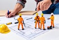 Miniature figures construction workers working on a blueprint. Suitable for architectural concepts, engineering designs