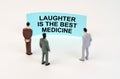 Miniature figures of people stand in front of a blue sign with the inscription - Laughter is the Best Medicine