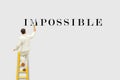 Miniature figurine character as painter standing on wooden ladder and painting to change the word Impossible to Possible.