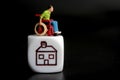 Miniature figurine of a disabled man on a wheelchair with the symbol of a house on a black background