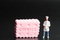 Miniature figurine of a chef standing in front of a huge pink cookie