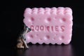 Miniature figurine of a dog standing in front of a huge pink cookie