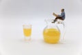 miniature figurine of a man sitting on a jug full of orange juice and reading a newspaper