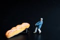 Miniature figurine of a man transporting a giant loaf of bread with a cart