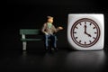 Miniature figurine of an old man sitting on a bench with the icon of a watch Royalty Free Stock Photo