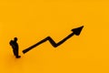 Miniature figurine posed as businessman in front of ascending graph arrow