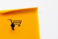 Miniature figurine posed as businessman looking at shopping cart handrawn on adhesive paper note