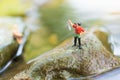 Miniature fisherman sitting on stone, fishing in the river. Macro view photo, use as a fishing career concept