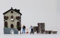 A miniature gay family standing between a miniature house and a pile of coins. Royalty Free Stock Photo