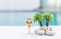 Miniature girl in orange bikini with coconut tree over blurred swimming pool background